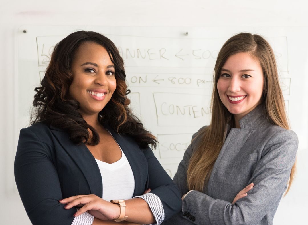 Female coach and client standing next to each other and looking satisfied about their partnership